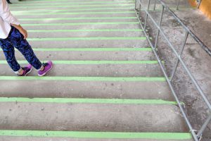 Legs of person standing looking down green-trimmed outdoor concrete stairs