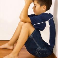 Unhappy boy sitting on floor in corner