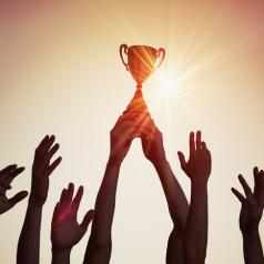 Silhouette of a trophy held above a crowd of reaching hands.
